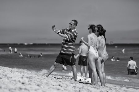 Asian man and three young women taking selfie in Miami's South Beach, Florida, USA, 2018 Asian man and three young women wearing swimwear taking selfie on beach, Miami Beach